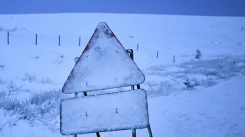A roadworks sign covered in snow. The fields behind it are also covered in snow