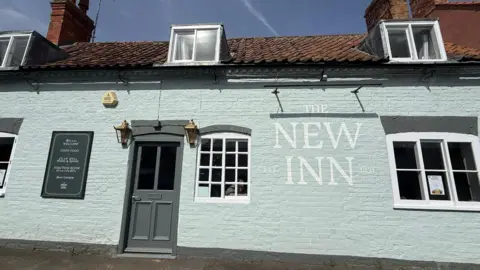 Neve Baker-Wright A pale blue painted pub with "The New Inn" painted on it in white.