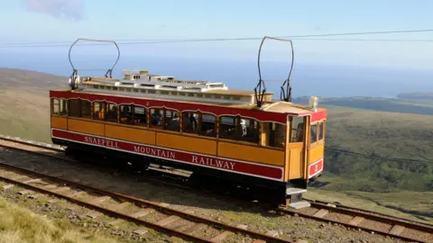 A snaefell mountain tram is high up on a hillside, in the distance you can see the sea.
