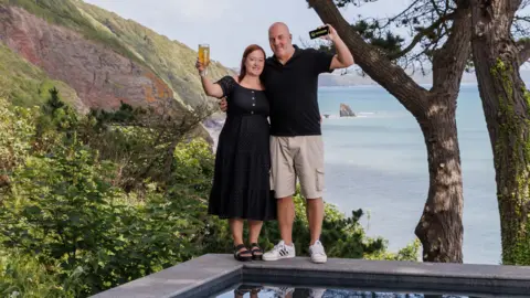 Omaze Darren Summers and wife Maria standing by the pool on their new beachside property in Cornwall
