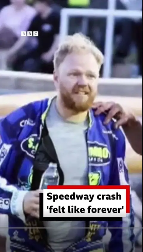 Rider Cameron Heeps walking away after the crash. His team are surrounding him. He is holding a bottle of water.