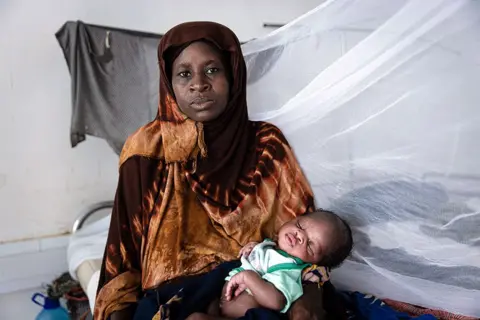   Alyona Synenko/ICRC Seorang ibu menggendong bayinya di lengannya di klinik penanganan kelaparan Palang Merah di kota Kismayo, Somalia