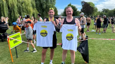 Two male race entrants, holding up white t-shirts with the Glos 10k logo on it