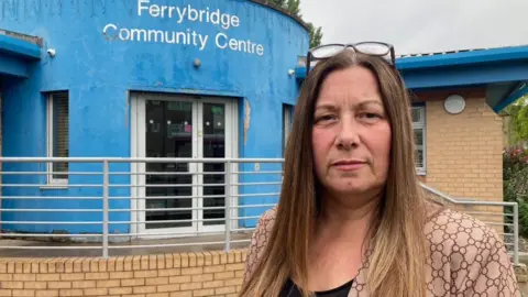 A woman with long, brown hair standing outside a community center which is painted light blue