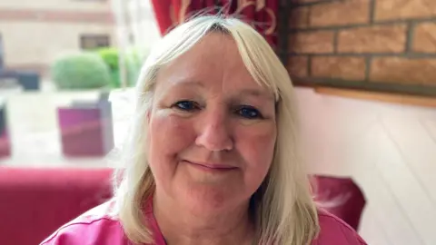 A head and shoulders photograph of Caroline Hughes. She is wearing a bright pink top.