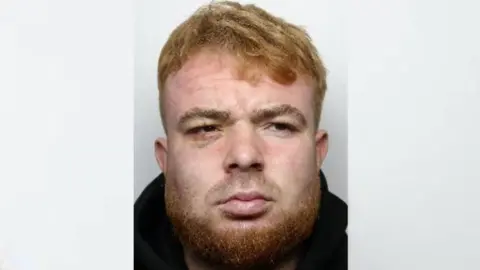 Police image of Henry Gaskin with short ginger hair, a short beard and wearing a black jumper. 