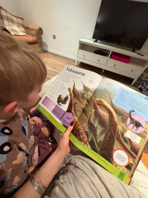 Charli Aitken Three-year-old Rudi. He is looking at a picture of a dinosaur in a book. 