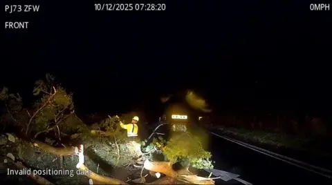 Bear Scotland A man in a high vis vest is seen chopping up a tree at night on the A84
