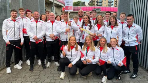 ERICA BELLHOUSE The Manx team posing in a group in their team tracksuits which are red and white, holding Manx flags.