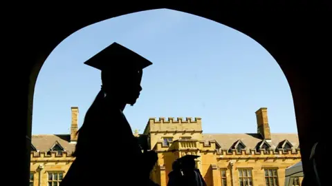 The silhouette of a graduating woman walking in front of a university building