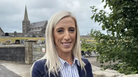 BBC Carla Lockhart, a woman with blonde hair, blue jacket and blue and white blouse, standing at Drumcree, near Portadown.