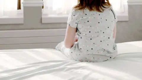 Anonymous child sitting on a why bed in front of windows