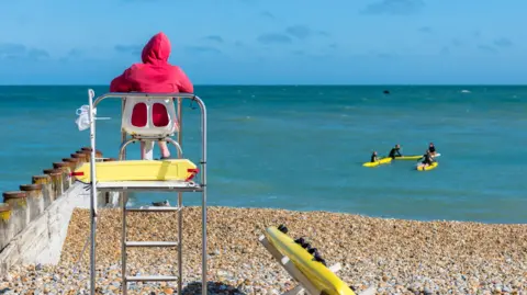 Rear view of a lifeguard sitting on a watchtower at the beach with surfers in the distance.