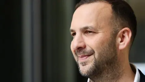 Reuters Green Party leader Zack Polanski has short brown hair and a beard. He is wearing a suit.