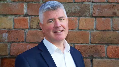 Scottish Information Commissioner A man with grey hair, wearing a dark blue suit and white shirt, looks at the camera in a close-up shot 