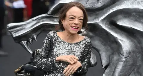 Getty Images Liz Carr wears a sparkly dress and smiles in a portrait photograph