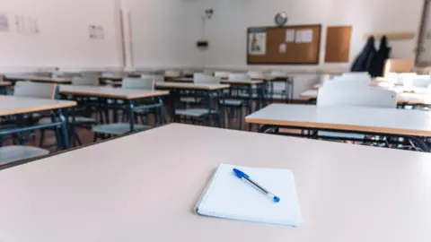 A empty classroom with a pad of paper and a pen on it