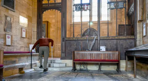 Josie Sturgess Mills Photography An elderly man with a walking stick stoops as he climbs three stone steps from the Lady Chapel, separated from the rest of the abbey by an ornate carved wooden screen.