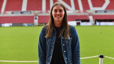 Vicki Eyles wearing a denim jacket standing in front of Swindon Town football grounds