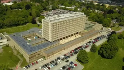 BBC An aerial view of County Hall in Norwich, a central tower block surrounded by smaller two and three-storey buildings and a car park.