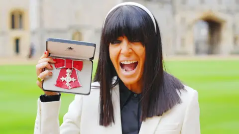 Reuters Claudia Winkleman grins with delight while holding up her MBE outside Windsor Castle