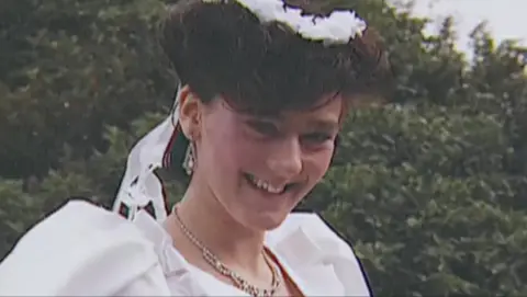 I Fought The Law recounts mum's double jeopardy murder law fight 3 Family handout Julie Hogg, who was murdered in 1989, smiles for a photograph. She is wearing a white dress with puffed shoulders, along with a white floral head decoration, and a silver necklace. In the background is shrubbery.