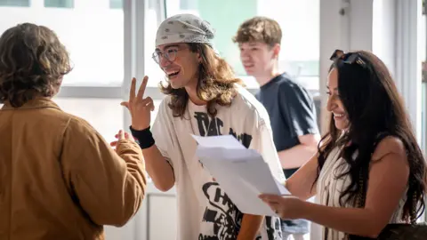 Getty Images A group of students gather around holding papers and gesturing to each other while reading their results at a high school in Cardiff on Thursday.