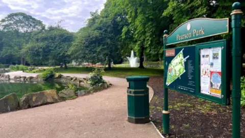 Hull City Council Pearson Park sign with a lake on the left and pathway surrounded by trees