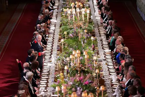 AFP King Charles addresses the banquet's guests, who line a long table covered in flowers, lamps and table-wear.