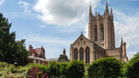 Getty Images A view of St Edmundsbury Cathedral. The large cathedral can be seen high above nearby buildings and towering over nearby trees.