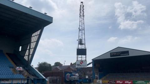 Floodlight in corner of ground, with crane preparing to take it down