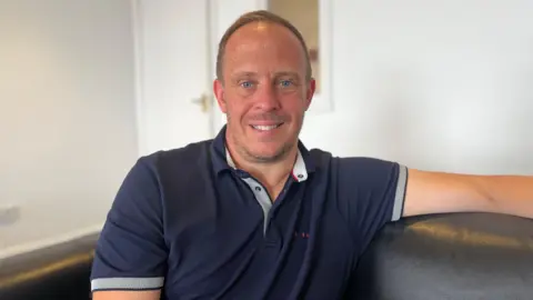 Man with short brown hair smiling at the camera. He's wearing a navy blue polo shirt.