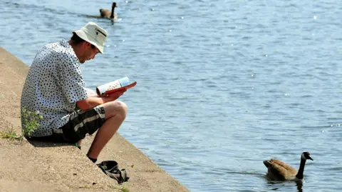 PA Media A man reading a book while geese swim past on the River Trent