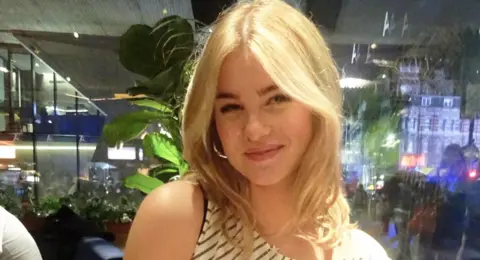 Gwen Shepherd Gwen pictured smiling at the camera. She is sitting in what looks like a restaurant.