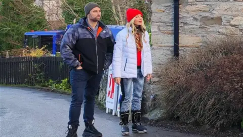 Actress Caprice stands alongside a crew member on location at a café in Aberfeldy.  