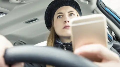 Getty Images Woman with long hair wearing black hat uses phone in lorry cab