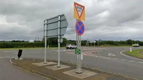 A junction on the A1 with roads joining the main road from both sides. A grey hatchback is driving past on the main carriageway.
