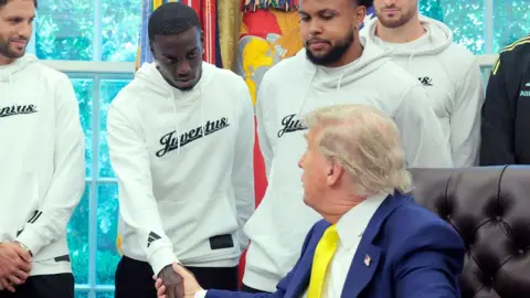 Getty Images President Donald Trump wearing a suit and a yellow ties shakes hands with Timothy Weah, wearing white jumper in the Oval Office - 18 June 2025.