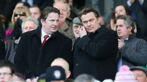Getty Images Two men at a football match, wearing dark overcoats