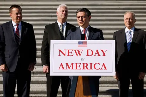 Getty Images House Speaker Mike Johnson stands behind a lectern with a sign that reads "new day in America"