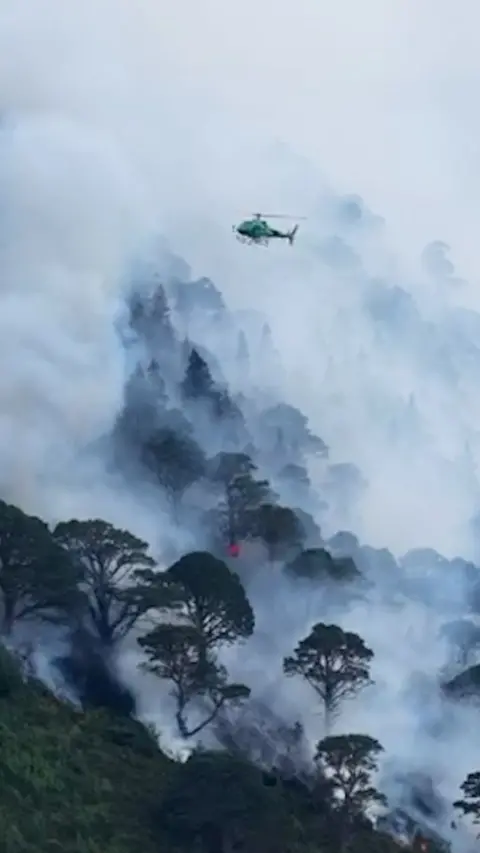 A helicopter flying over a wildfire in the Cairngorms