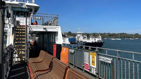 One of the ferries on the Torpoint Ferry service goes past another vessel operating on the chain ferry. It is a sunny day.