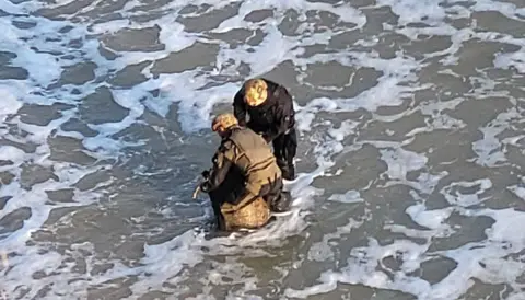 Two men carry a sea mine through the waves near the shore of the Black Sea