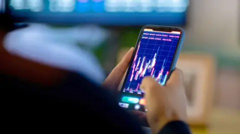 A man looks at a trading screen on his mobile phone 
