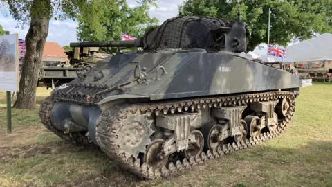 Luke Deal/BBC A Sherman tank rests in a grass field at the Suffolk Show. It is a camouflage colour.