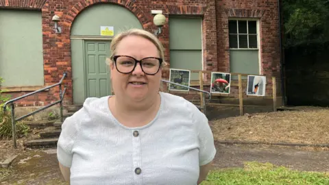 Photograph of Sam Elliott from Bolton Council. She is pictured in front of Rock Hall in the Moses Gate Country Park in Farnworth.