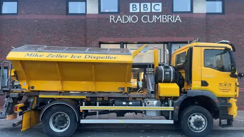 The gritter, a big yellow truck the words "Mike Zeller Ice Dispeller" emblazoned on the side, outside the BBC Radio Cumbria offices.