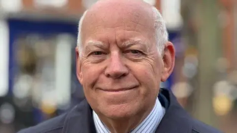 A picture of West Berkshire Council leader Jeff Brooks standing on Newbury's Northbrook Street. He's wearing a blue and white striped shirt and a striped tie.