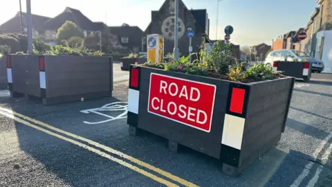 A planter placed on a road which has road closed written on it as part of the trial