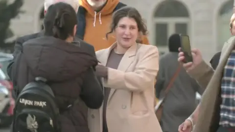 Reuters Bella Culley is walking down the surrounded by people. She is wearing a biege coat and a maroon top.